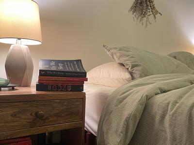 A nightstand with four books next to a bed