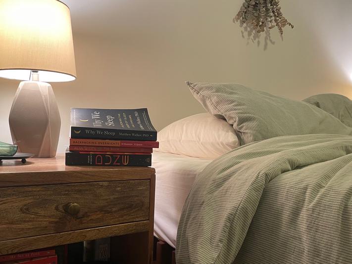 A nightstand with four books next to a bed